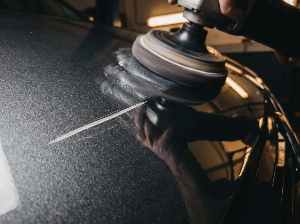 Machine polisher removing a scratch from black car paint