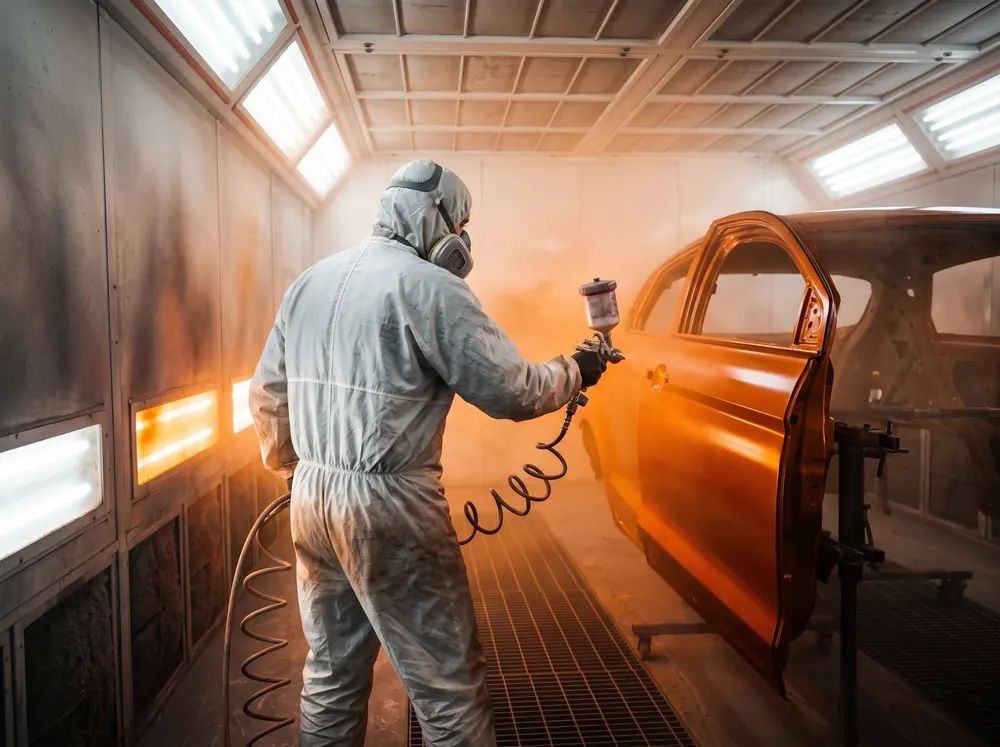 Painter in a protective suit spraying a car door in the Malaga paint booth